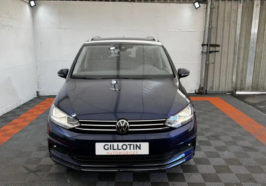 Vue avant d'un Volkswagen Touran bleu 2024 avec calandre chromée et phares LED dans un garage.
