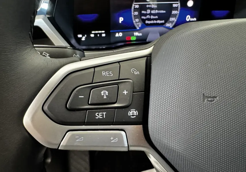 Gros plan sur les commandes de régulateur de vitesse au volant cuir du Volkswagen Touran 2024, affichage numérique en arrière-plan.