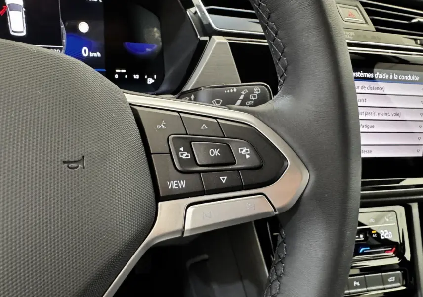 Gros plan sur le volant cuir noir du Volkswagen Touran 2024 avec commandes multifonctions et tableau de bord digital.