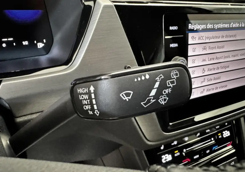 Gros plan sur la commande des essuie-glaces dans l’habitacle du Volkswagen Touran 2024, écran tactile en arrière-plan.