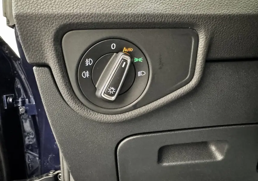 Gros plan sur le bouton de commande des phares à gauche du tableau de bord d’un Volkswagen Touran bleu 2024.