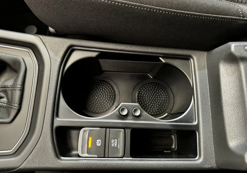 Gros plan sur la console centrale noire du Volkswagen Touran 2024 avec porte-gobelets et frein à main électrique allumé.