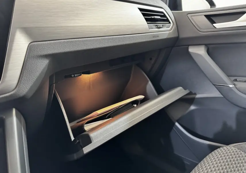 Gros plan sur la boîte à gants ouverte côté passager du Volkswagen Touran 2024 avec éclairage intérieur et tableau de bord gris.