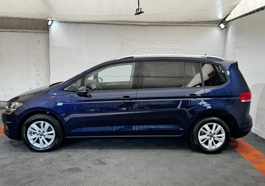 Volkswagen Touran bleu 2024 vue de profil côté gauche dans un espace intérieur éclairé.