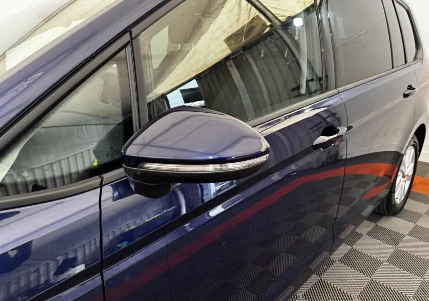 Vue rapprochée côté gauche du Volkswagen Touran bleu 2024, mettant en valeur la portière et le rétroviseur avec clignotant intégré.