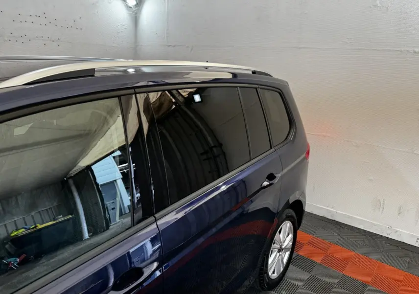 Vue latérale droite du Volkswagen Touran bleu 2024, avec vitres teintées et barres de toit chromées visibles.