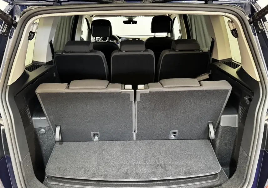 Vue arrière du coffre ouvert du Volkswagen Touran bleu 2024, montrant la troisième rangée de sièges rabattables.