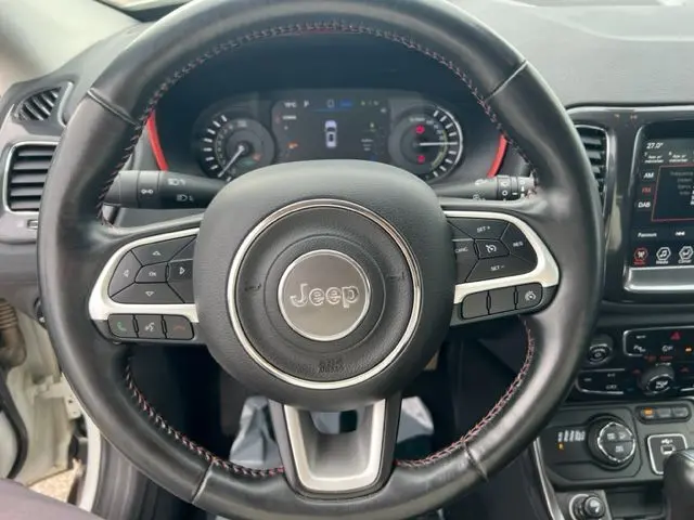 Vue rapprochée du volant en cuir noir avec surpiqûres rouges du Jeep Compass hybride rechargeable blanc de 2020.