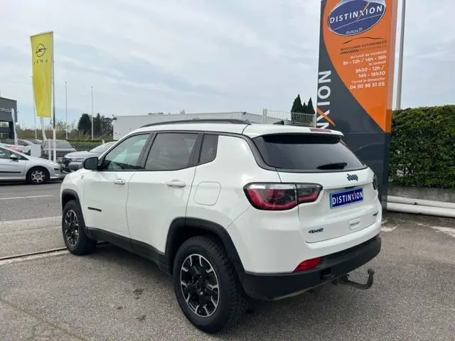 Vue 3/4 arrière gauche d'un Jeep Compass blanc hybride rechargeable 2020 avec attelage et jantes noires.