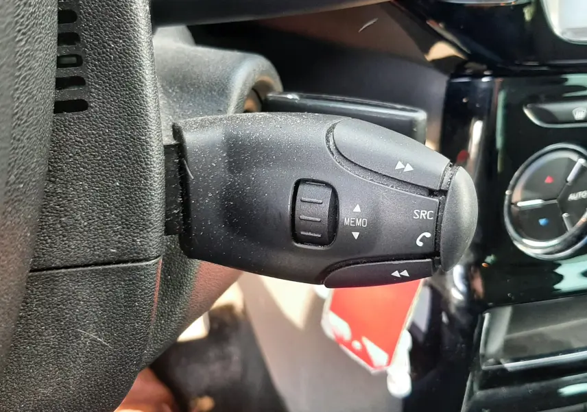 Gros plan sur la commande au volant côté gauche d'une Citroën C3 noire, avec tableau de bord et climatisation en arrière-plan.