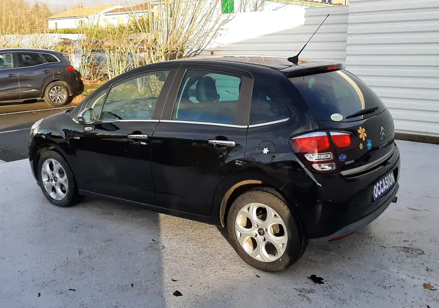 Citroën C3 noire vue de trois quarts arrière droit, avec stickers colorés sur le hayon et plaque "OCCASION".