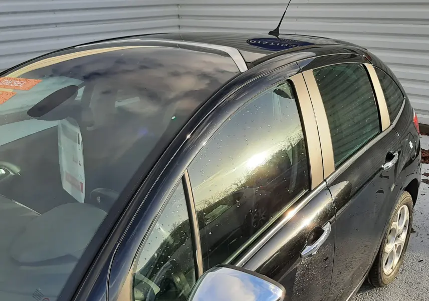 Vue 3/4 avant droit d'une Citroën C3 noire 2016 avec rétroviseur chromé et toit panoramique visible.