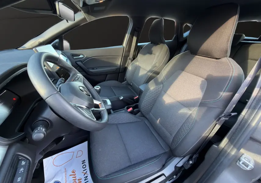 Vue intérieure côté conducteur du Renault Captur 2024, sièges gris avec surpiqûres bleues et volant multifonction.