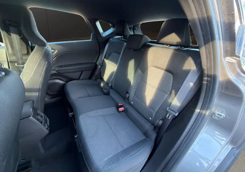 Vue intérieure côté arrière droit du Renault Captur 2024 gris Cassiopée, montrant les sièges arrière en tissu avec surpiqûres bleues.
