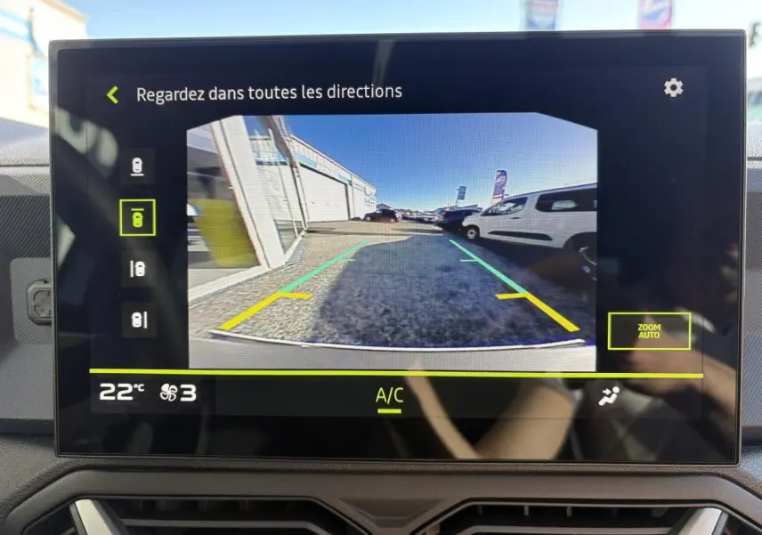 Écran tactile montrant la caméra de recul du Dacia Duster blanc métallisé, vue arrière avec lignes de guidage colorées.