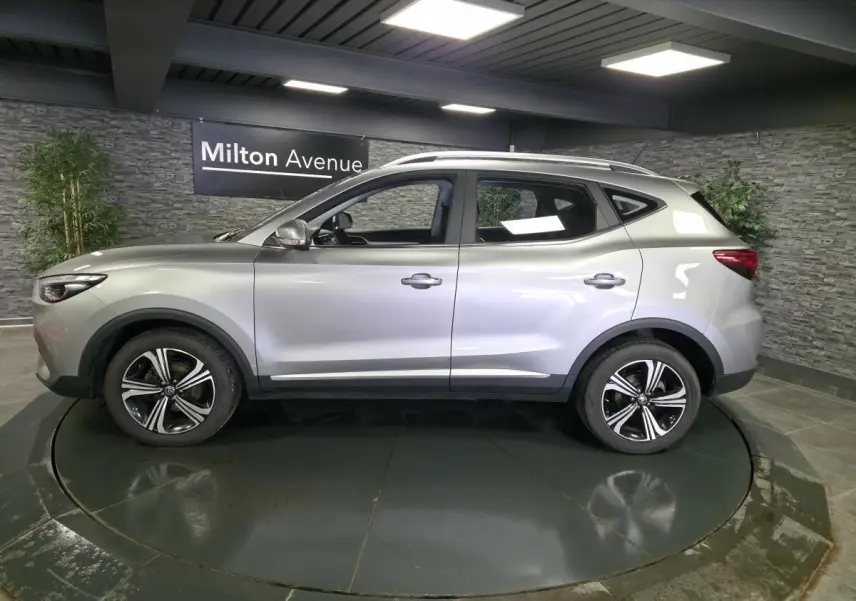 Vue de profil côté gauche du SUV MG ZS gris métallisé avec jantes alliage 17 pouces dans un showroom.