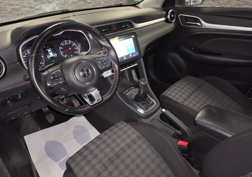 Intérieur de MG ZS 2023 vu côté conducteur, volant cuir, console centrale avec écran tactile et levier de vitesses manuel.
