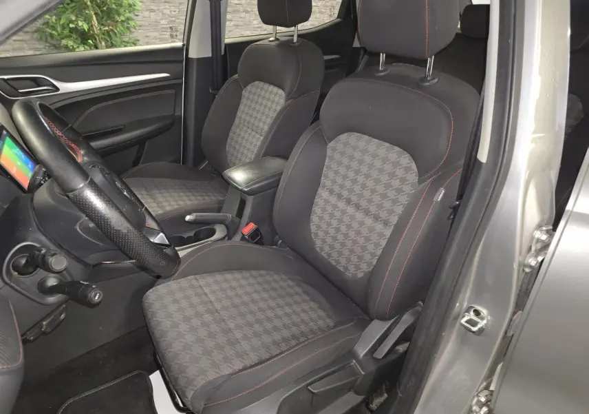 Vue intérieure côté conducteur du MG ZS gris 2023, sièges tissu à motif pied-de-poule et volant cuir avec surpiqûres rouges.