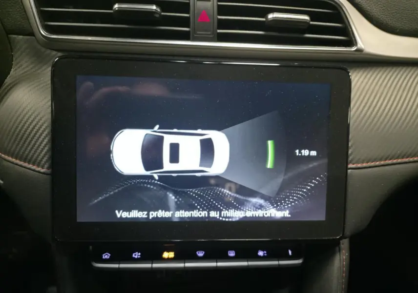 Écran tactile intérieur montrant l'alerte de distance de stationnement du MG ZS gris, avec tableau de bord en carbone.