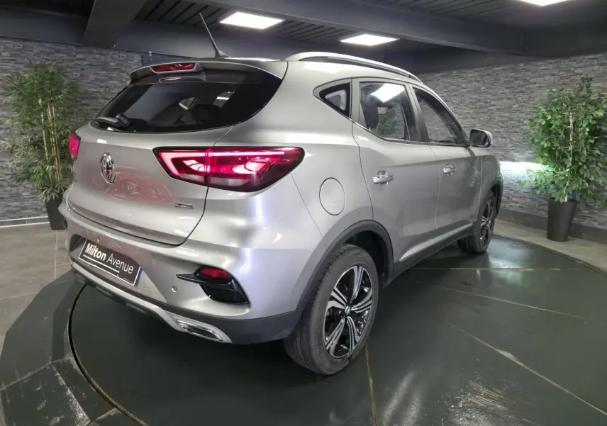 Vue 3/4 arrière droite du SUV MG ZS gris métallisé avec feux arrière LED allumés et jantes alliage noires.