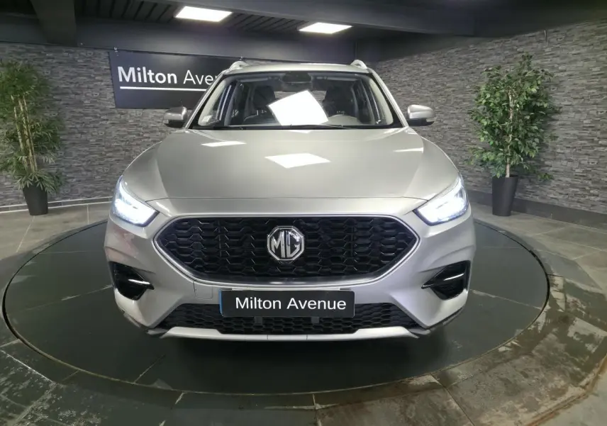 Vue avant du MG ZS gris métallisé 2023 avec calandre noire hexagonale et phares LED allumés.