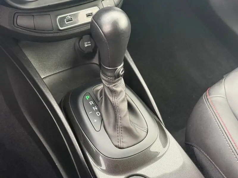 Gros plan sur le levier de vitesses automatique en cuir noir de la FIAT 500X 2024, avec console et sièges gris à surpiqûres rouges.