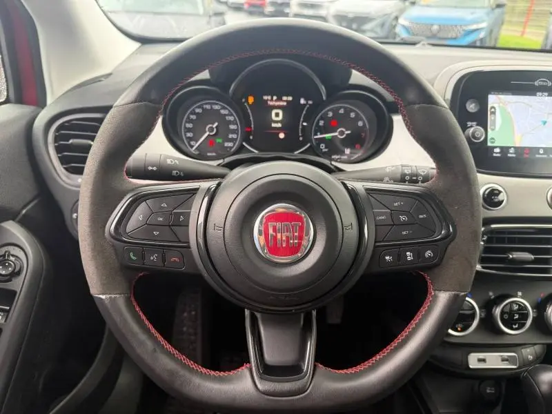 Vue rapprochée du volant en alcantara avec surpiqûres rouges du Fiat 500X 2024, tableau de bord et écran tactile visibles.