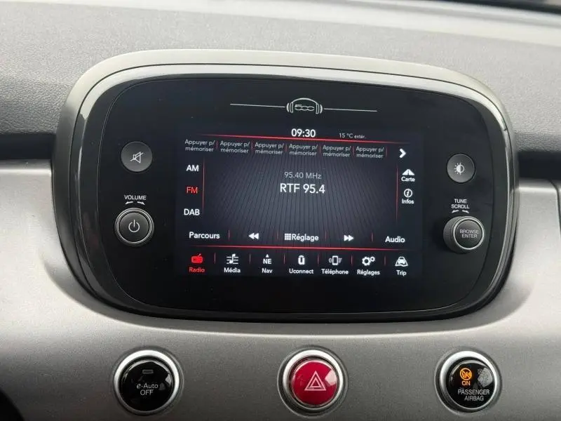 Écran central tactile de la FIAT 500X 2024 affichant la radio FM, entouré de boutons de contrôle sur tableau de bord gris.