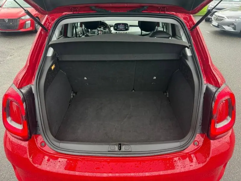 Coffre ouvert vu de l'arrière d'une FIAT 500X 2024 Rouge Passione pastel, intérieur noir et tableau de bord visible.