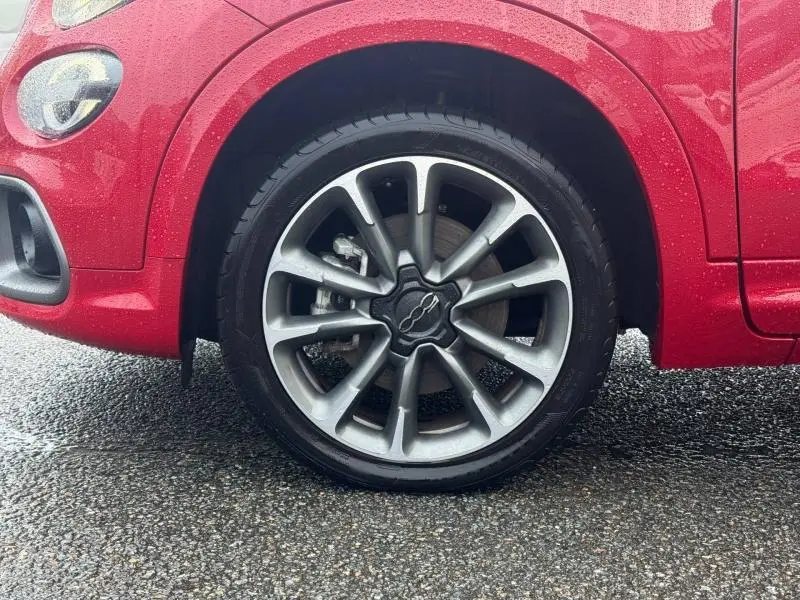 Gros plan sur la roue avant gauche du FIAT 500X rouge Passione pastel avec jante alliage distinctive sous la pluie.