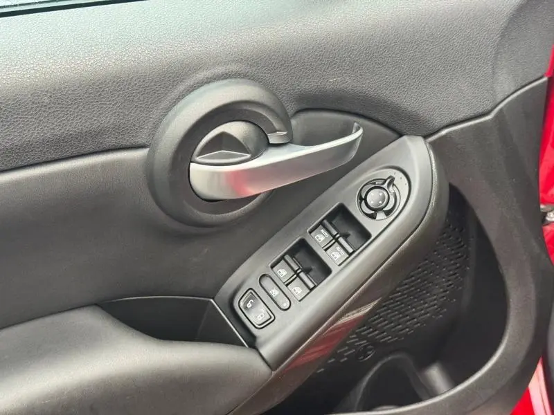 Gros plan sur la poignée intérieure et les commandes des vitres côté conducteur d’un FIAT 500X Rouge Passione pastel 2024.