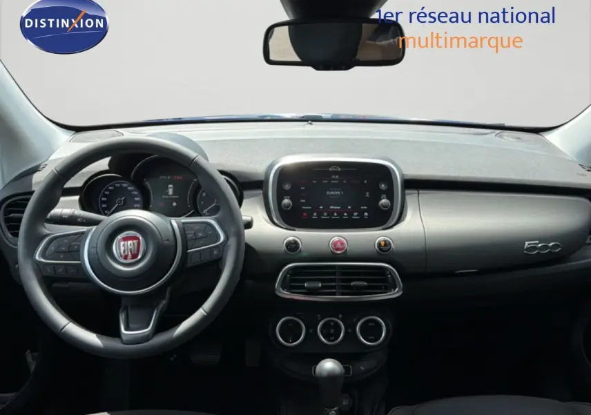 Vue intérieure frontale du tableau de bord et volant de la Fiat 500X 2024 en bleu Venezia, avec écran tactile central et commandes intégrées.