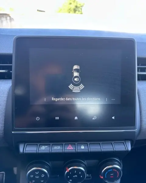 Écran tactile central de la Renault Clio V gris, affichant l'aide au stationnement avec message "Regardez dans toutes les directions".