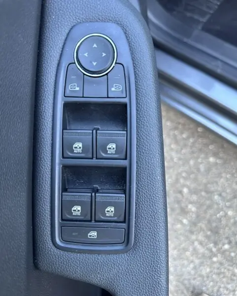 Gros plan sur les commandes des vitres électriques et des rétroviseurs côté conducteur d'une Renault Clio gris 2025.