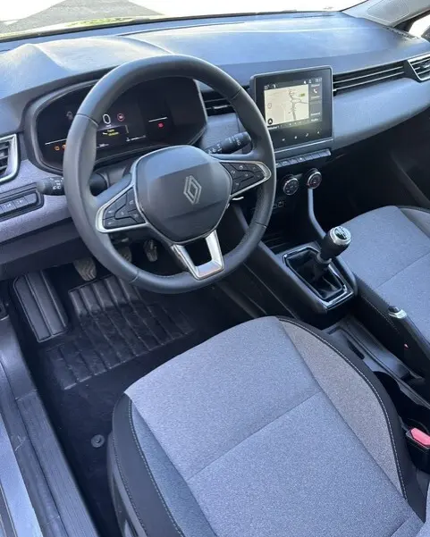 Vue intérieure côté conducteur de la Renault Clio gris 2025, avec volant multifonction, écran tactile et boîte manuelle.