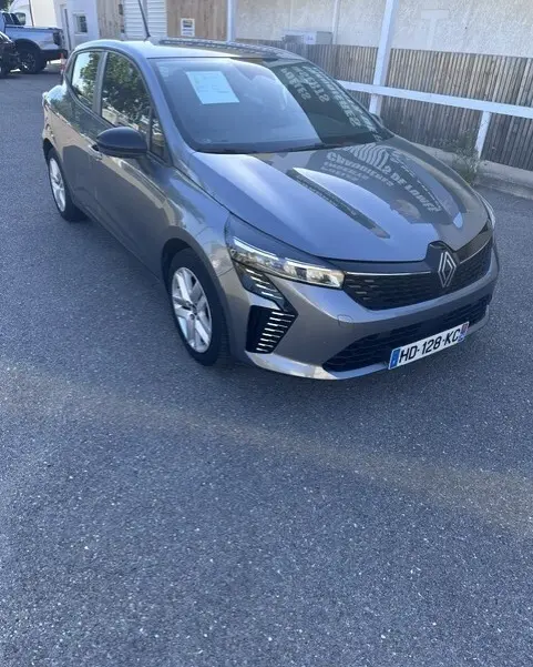 Renault Clio gris 2025 vue 3/4 avant droit, avec calandre moderne et feux LED distinctifs.