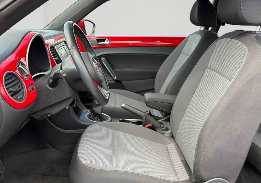 Intérieur côté conducteur de la Volkswagen Coccinelle 2012, tableau de bord rouge Tornade et sièges gris.