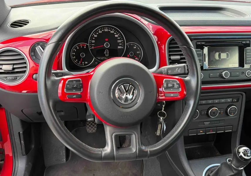 Vue intérieure du volant cuir noir et rouge de la Volkswagen Coccinelle 2012 avec tableau de bord et levier de vitesse manuel.