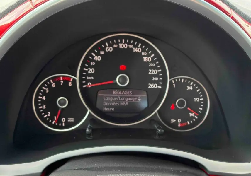 Vue rapprochée du tableau de bord de la Volkswagen Coccinelle rouge, affichant les compteurs et l'écran de réglages.