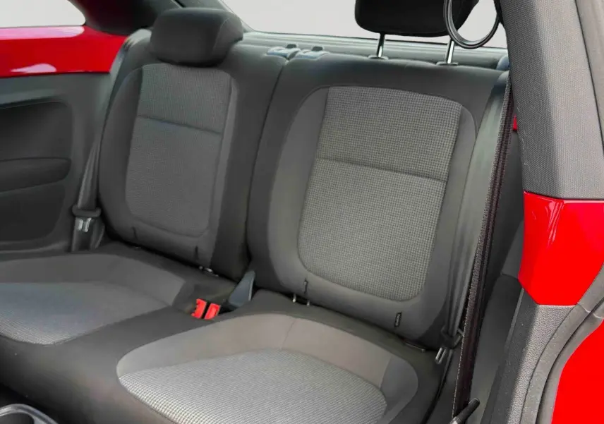 Vue intérieure arrière droite de la Volkswagen Coccinelle rouge, montrant les sièges arrière gris et la carrosserie rouge Tornade.