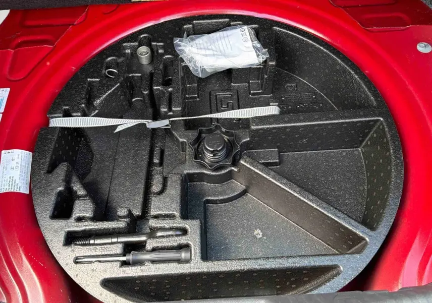 Vue plongeante sur le coffre à outils vide de la Volkswagen Coccinelle rouge, montrant l'emplacement des accessoires.