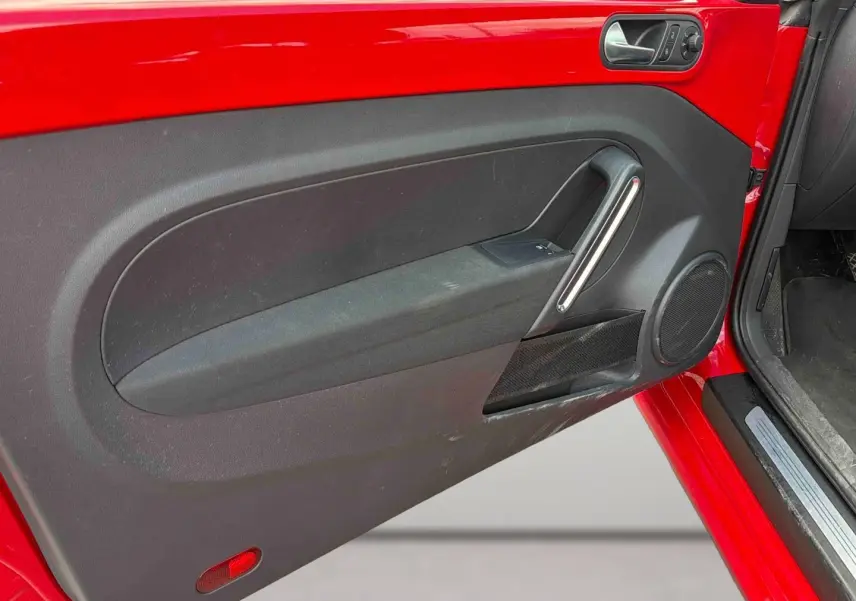 Vue rapprochée de la porte avant gauche rouge de la Volkswagen Coccinelle 2012 avec panneau intérieur noir et poignée argentée.