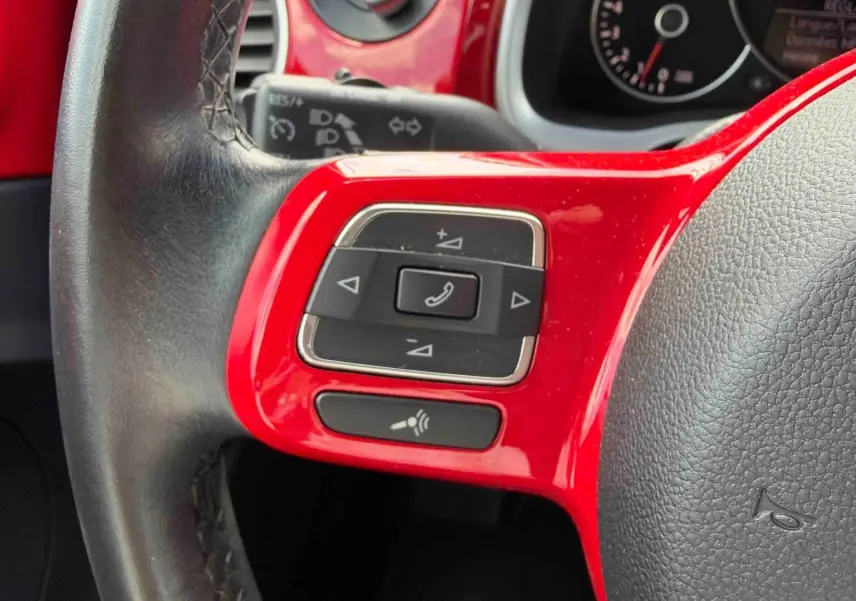 Gros plan sur la partie gauche du volant rouge et noir de la Volkswagen Coccinelle avec commandes multifonctions.