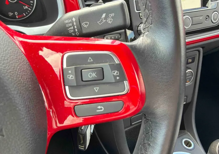 Gros plan sur le volant cuir multifonction rouge et noir de la Volkswagen Coccinelle avec commandes intégrées.
