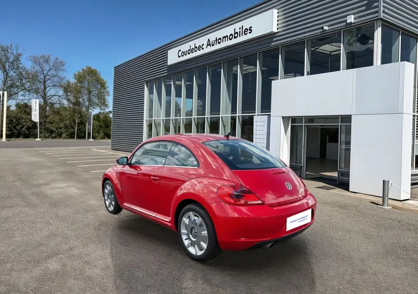 Volkswagen Coccinelle rouge vue en 3/4 arrière droit, avec jantes 18 pouces et feux arrière LED, devant un showroom.
