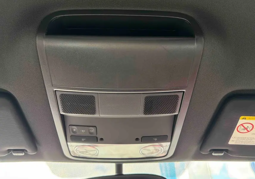 Vue intérieure du plafonnier avant de la Volkswagen Coccinelle rouge, montrant les commandes d’éclairage et les haut-parleurs intégrés.