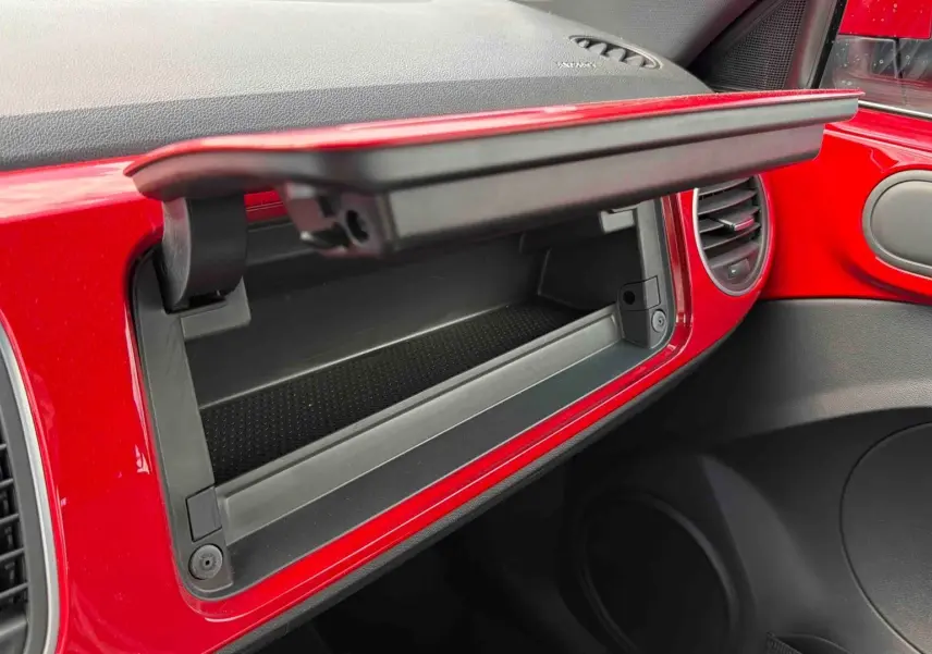 Gros plan intérieur sur la boîte à gants ouverte entourée de la planche de bord rouge vif de la Volkswagen Coccinelle 2012.