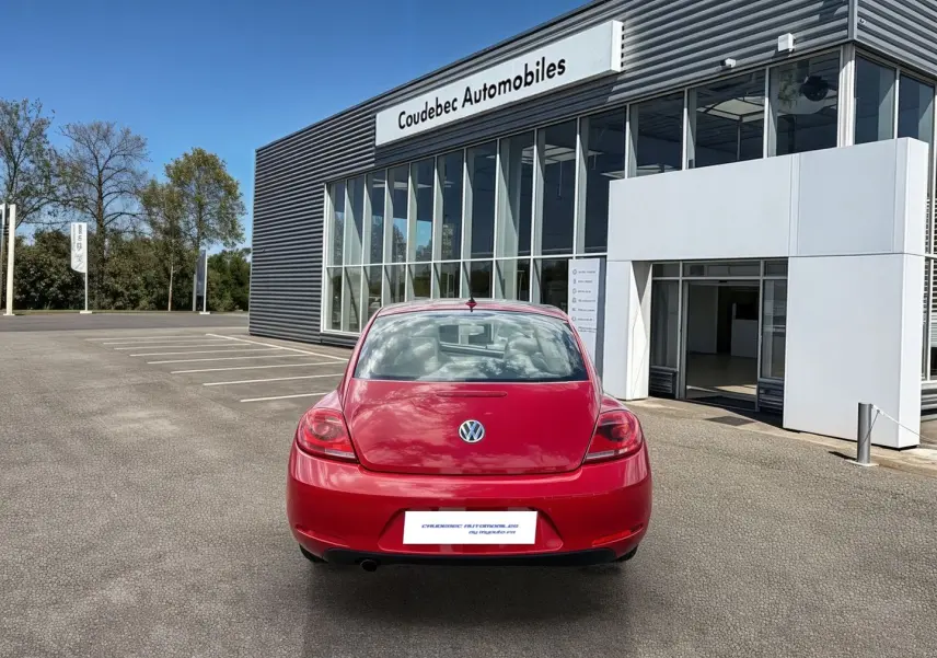Vue arrière d'une Volkswagen Coccinelle rouge Tornade garée devant un bâtiment moderne de concession automobile.