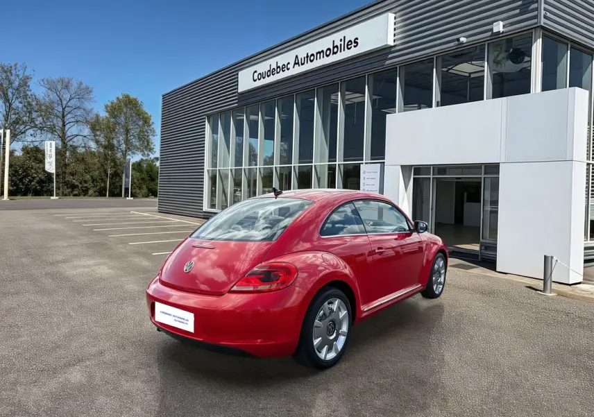 Volkswagen Coccinelle rouge vue 3/4 arrière droit, avec jantes 18 pouces et feux arrière LED, devant un showroom.