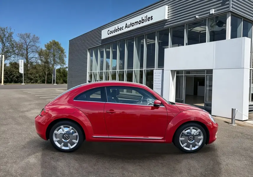 Vue de profil droit d'une Volkswagen Coccinelle rouge Tornade avec jantes 18 pouces Disc, stationnée devant un concessionnaire.